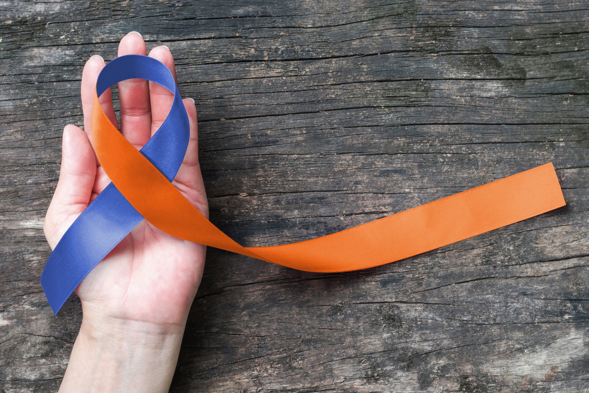 Human rights for family caregivers awareness in orange navy blue fabric ribbon on human hand old aged background